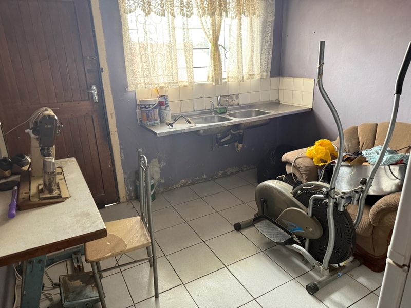 A functional scullery or utility area featuring a stainless steel double sink, tiled splashback, and tiled flooring, currently in need of maintenance and cosmetic updates.