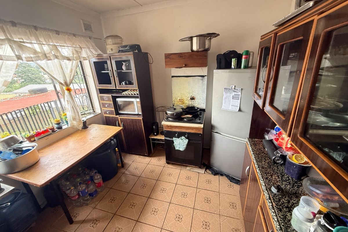 A functional kitchen featuring dark wood cabinetry, granite countertops, tiled flooring, and a freestanding stove, offering potential for modernization.