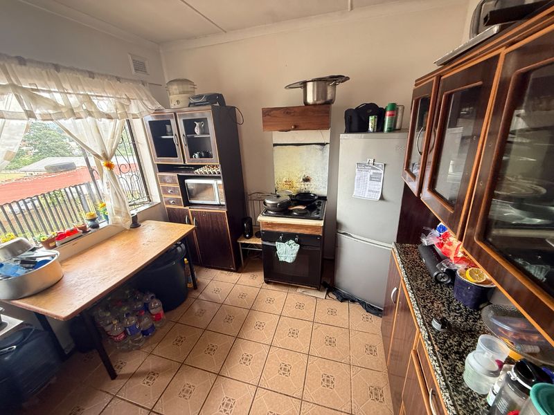 A functional kitchen featuring dark wood cabinetry, granite countertops, tiled flooring, and a freestanding stove, offering potential for modernization.