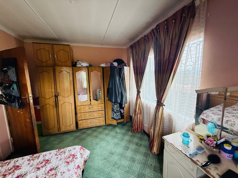 A bedroom featuring built-in wooden cupboards, security bars on the windows, and tiled flooring, offering a functional space with potential for modernization.