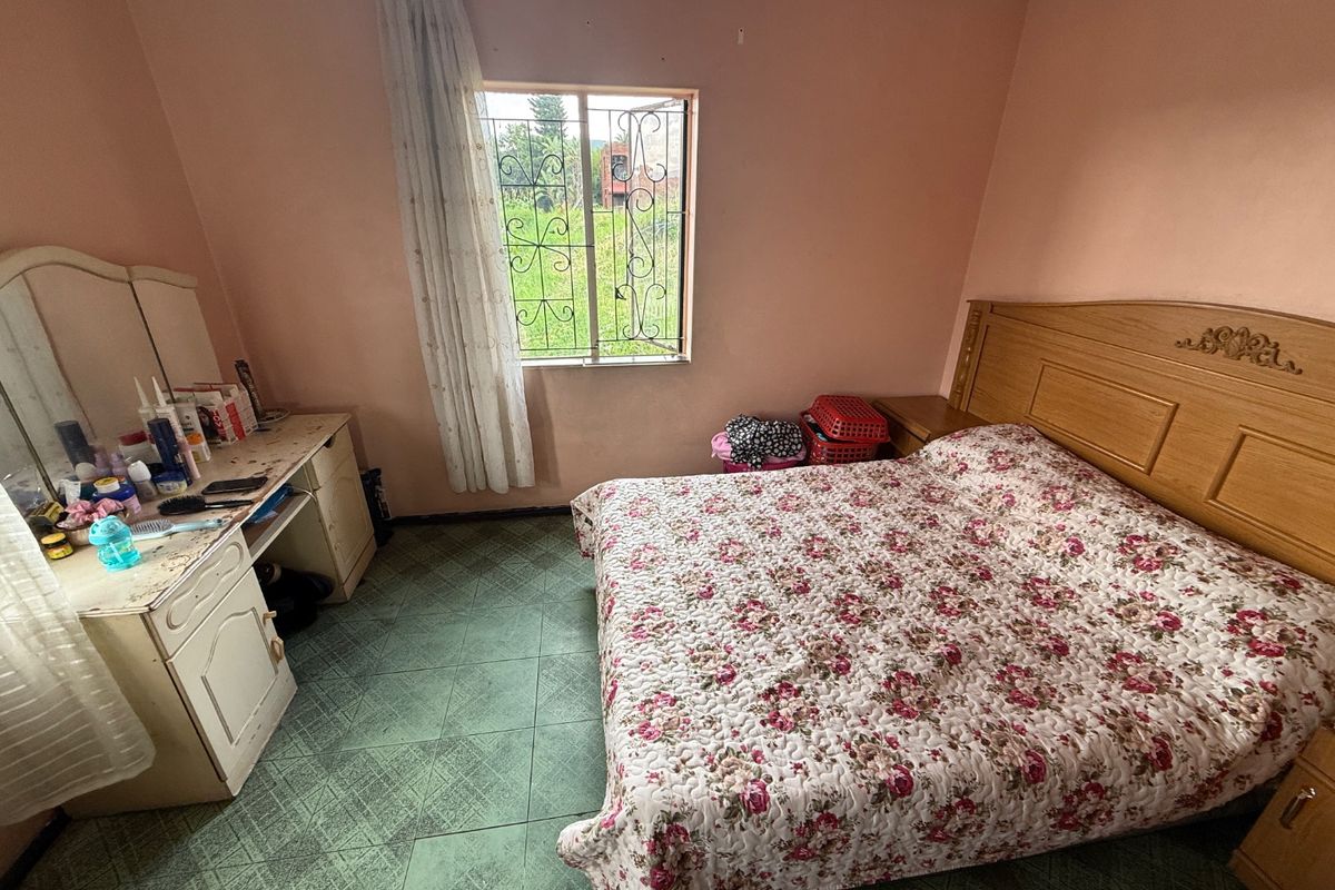 A bedroom featuring tiled flooring and a window with security bars, offering a functional space with potential for cosmetic updates.