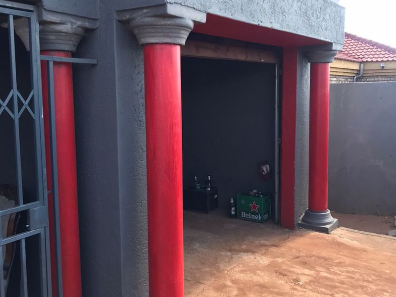 A garage exterior featuring decorative red columns and a security gate, with an open entrance leading to an unfinished interior space.