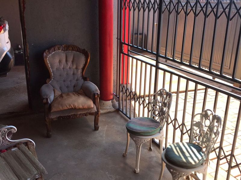 A covered patio area featuring a security gate, concrete flooring, and a decorative column, providing a functional outdoor space.