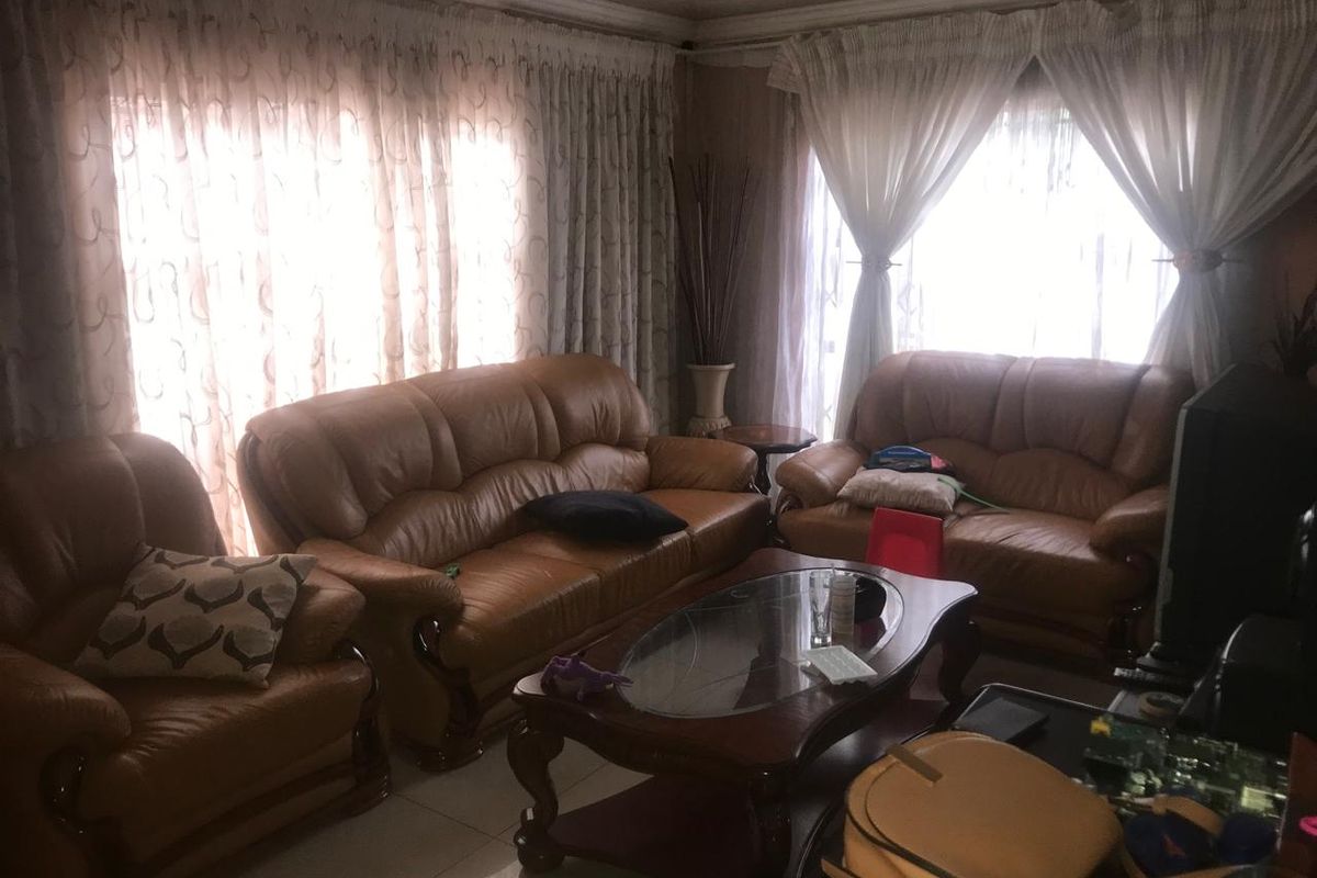 A living room area featuring tiled flooring and large windows with installed curtain tracks, providing natural light to the space.