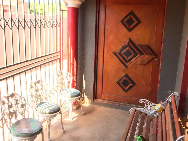 A covered patio area featuring a decorative wooden entrance door, security gate, and concrete flooring.