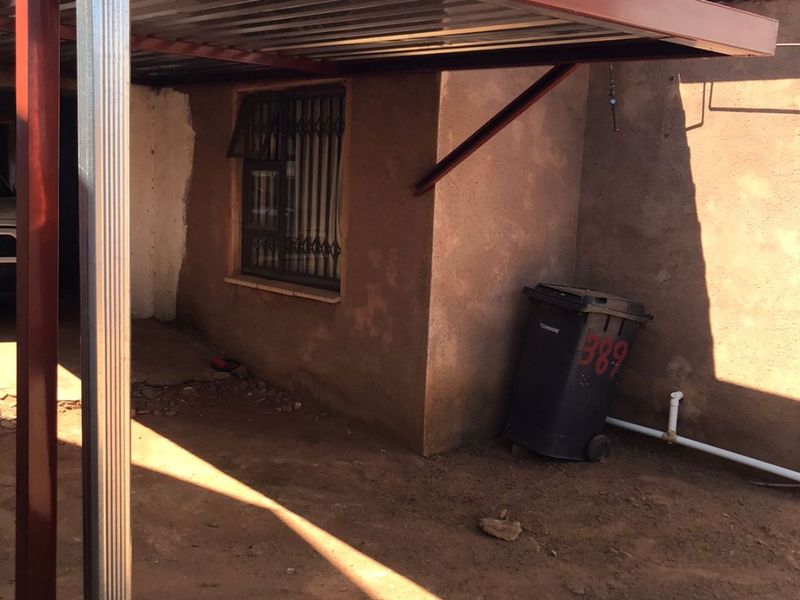 Rear exterior area featuring a metal carport structure, security burglar bars on the window, and exposed exterior wall finish.