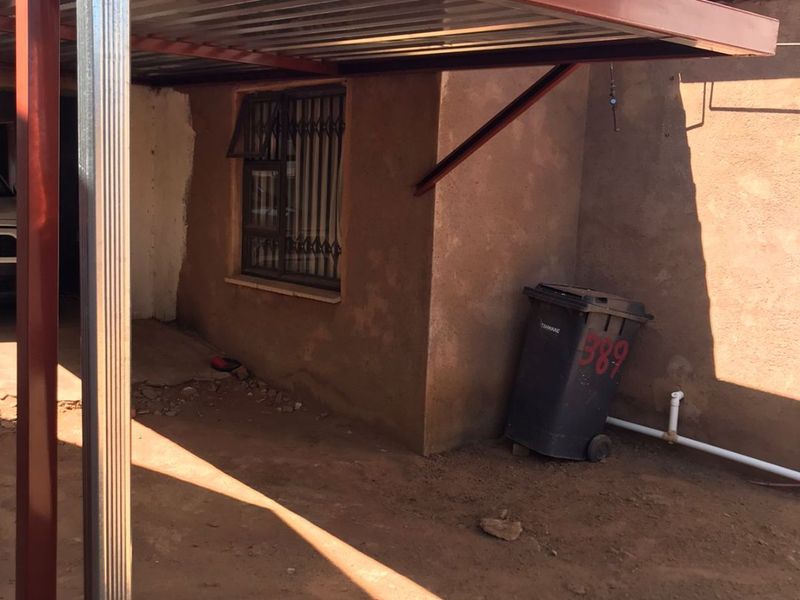 Rear exterior area featuring a metal carport structure, security bars on the window, and exposed exterior wall finish.