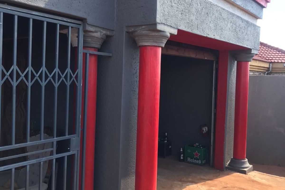 Exterior view of a garage featuring decorative red columns, a security gate, and a paved driveway area.