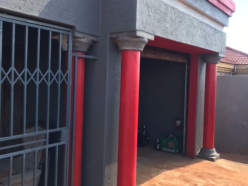 Exterior view of a garage featuring decorative red columns, a security gate, and a paved driveway area.