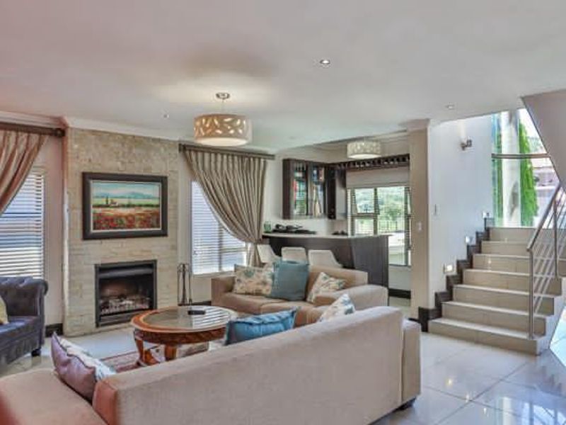 Spacious open-plan living area featuring a stone-clad fireplace, a built-in bar, and a modern staircase with a glass balustrade.