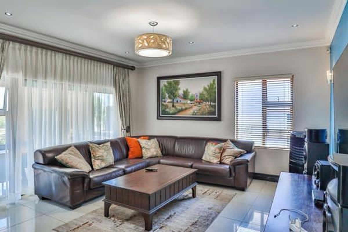 A well-maintained living room featuring tiled flooring, recessed downlighting, and large windows with venetian blinds and curtain tracks.