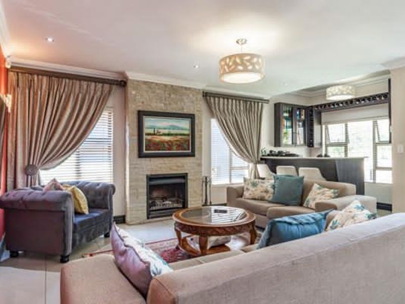 Spacious open-plan living area featuring a stone-clad fireplace, built-in bar, tiled flooring, and elegant crown molding throughout.