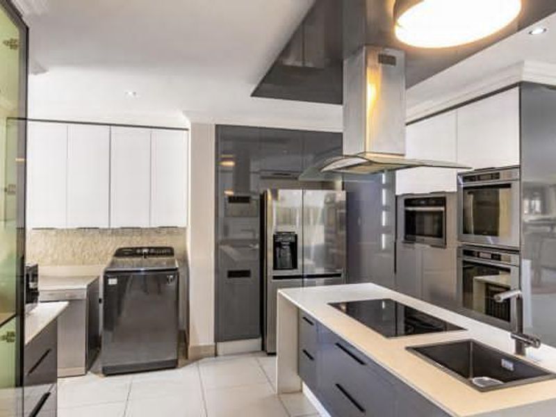 Modern kitchen featuring a central island with induction hob and sink, high-gloss cabinetry, and integrated stainless steel appliances.