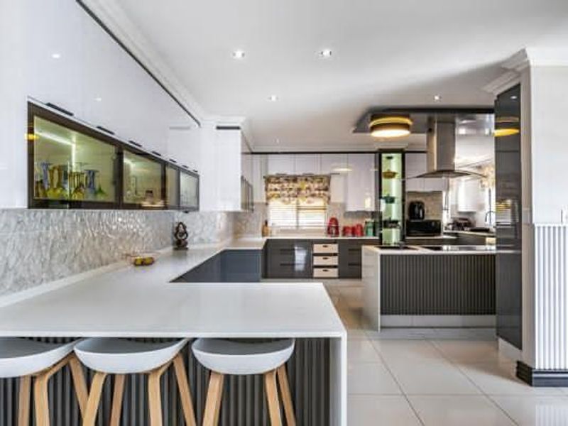 Modern, high-end kitchen featuring sleek glossy cabinetry, stone countertops, a central island, and integrated lighting, offering a sophisticated and functional culinary space.