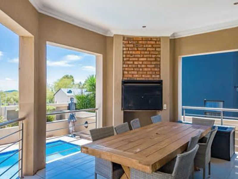 Covered outdoor patio featuring a built-in braai, brick feature wall, and stainless steel balustrades, overlooking the swimming pool area.