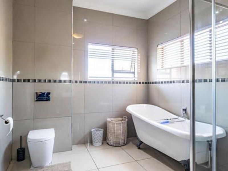 A modern bathroom featuring a freestanding bathtub, a glass-enclosed shower, and neutral floor-to-ceiling wall tiles.