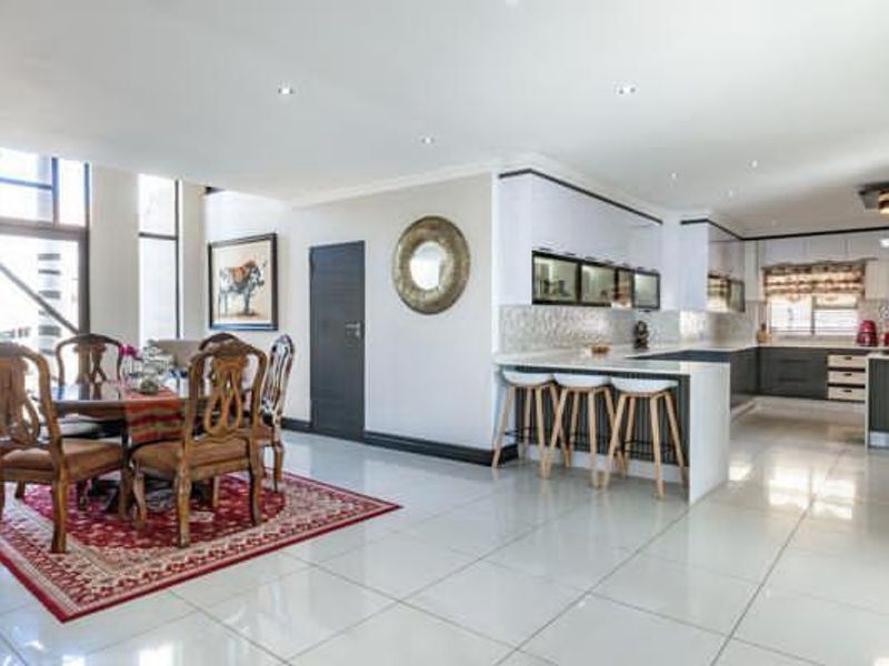 Spacious open-plan living and dining area featuring a modern kitchen with a breakfast bar, tiled floors, and abundant natural light from large windows.