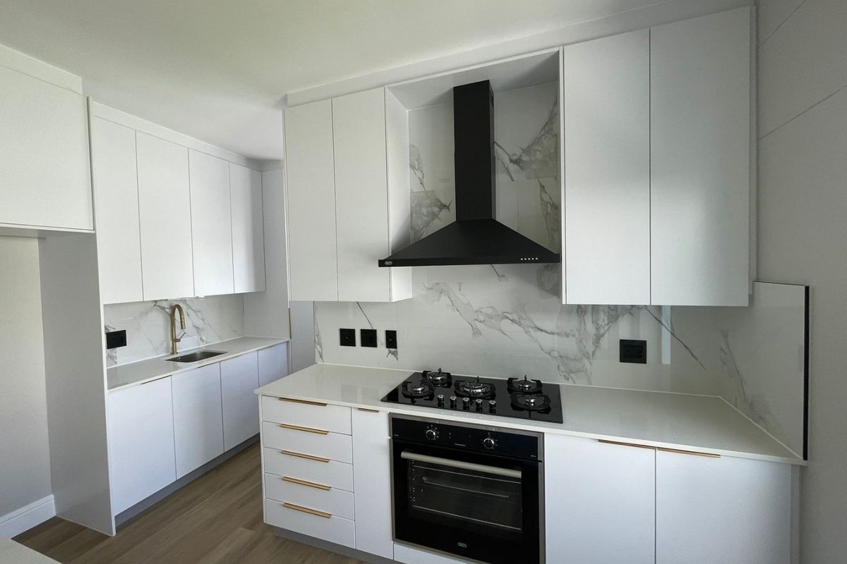 Modern kitchen featuring white cabinetry, stone countertops, marble-look splashback, gas hob, built-in oven, and high-quality brass fixtures.