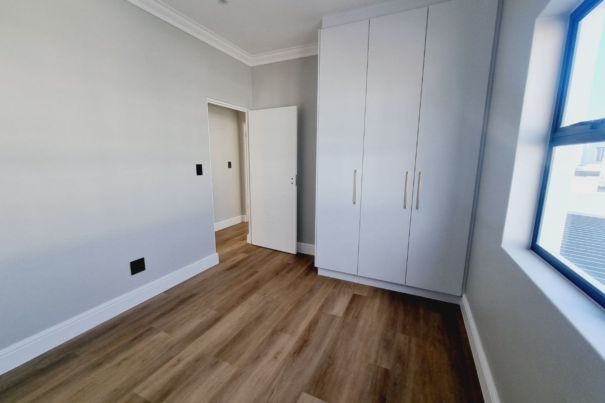 A bright, modern bedroom featuring neutral walls, high-quality laminate flooring, and ample built-in cupboard storage.
