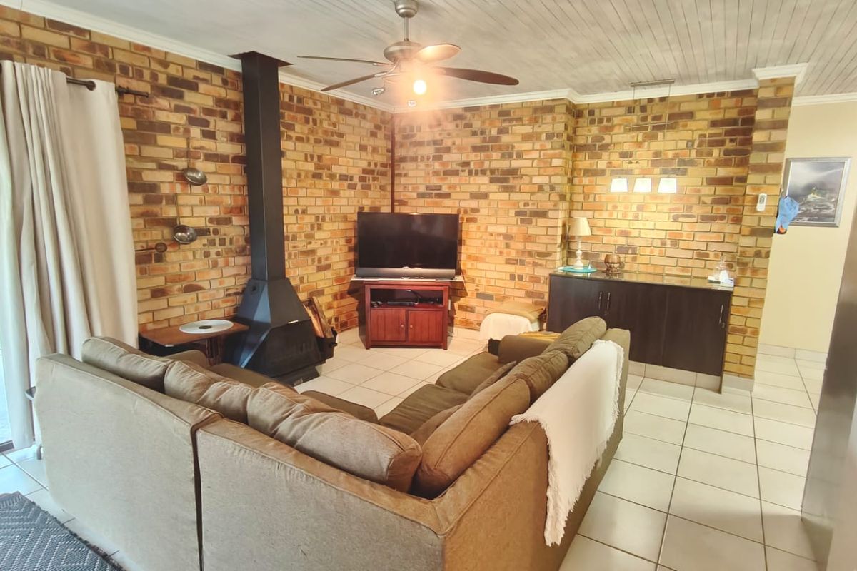 A cozy living room featuring exposed brick walls, a freestanding fireplace, tiled flooring, and direct access to the outdoor area through sliding glass doors.