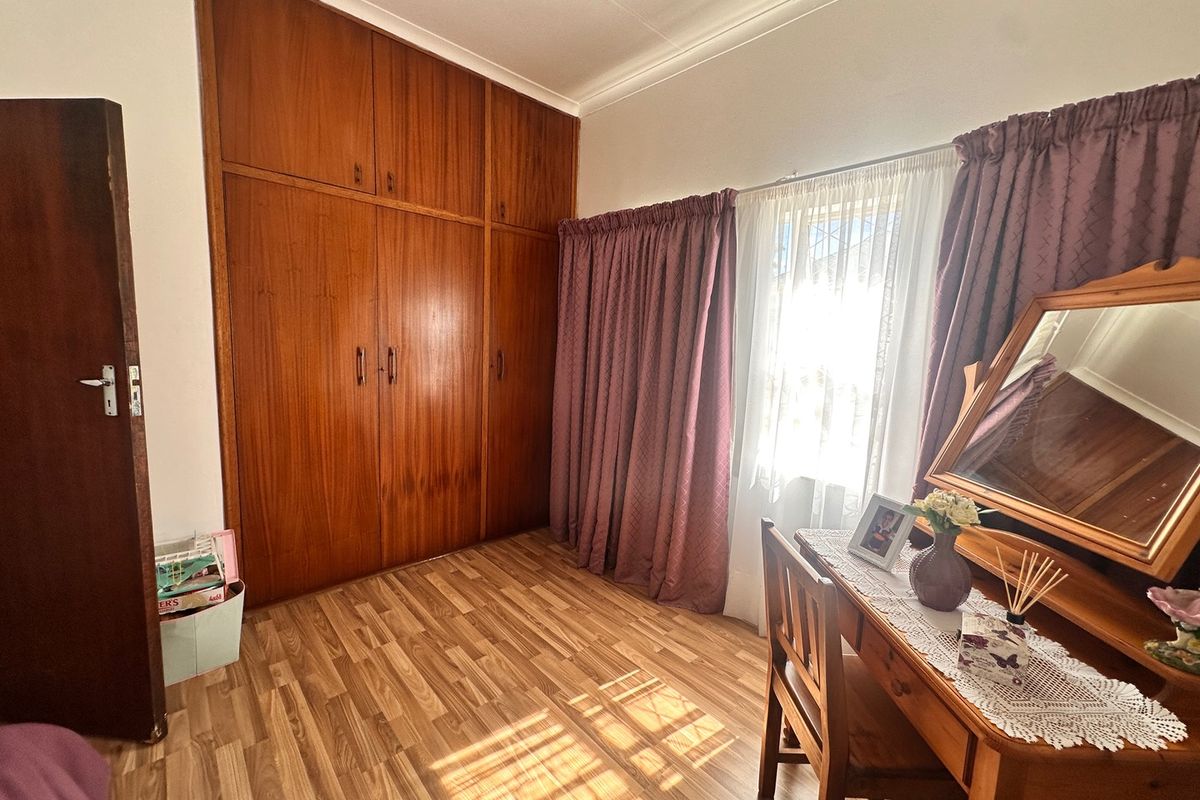 A bedroom featuring built-in wooden cupboards, laminate flooring, and a window with curtains.