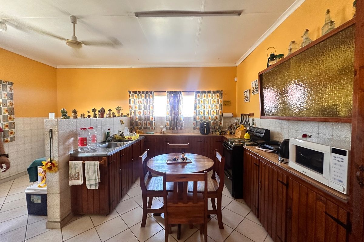 A dated kitchen featuring wooden cabinetry, tiled splashbacks, and ceramic flooring, offering a functional layout with space for a small dining area.