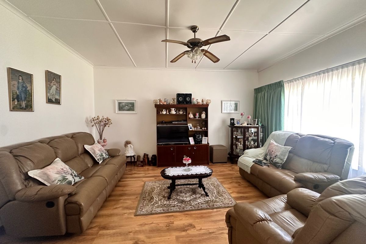 A spacious living room featuring laminate flooring, a central ceiling fan, and large windows with curtain tracks, offering a comfortable and functional living space.
