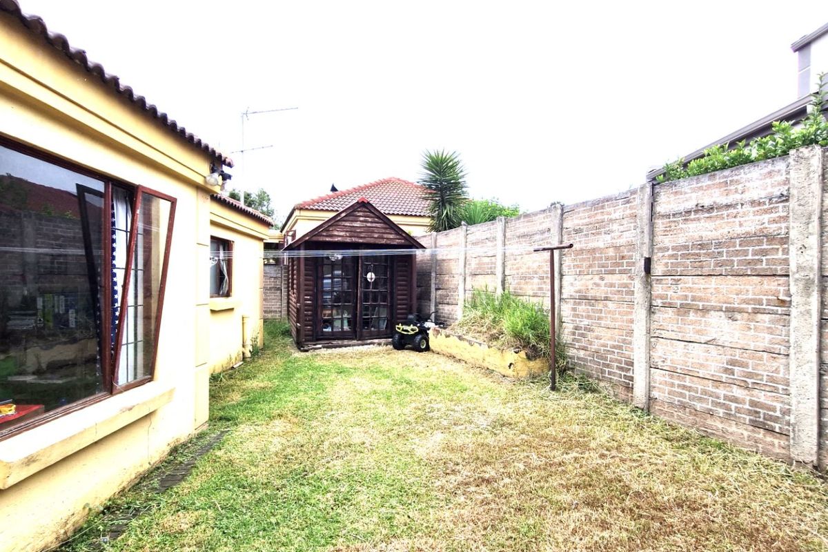 Rear garden area featuring a lawn, brick boundary wall, and a detached wooden garden shed.