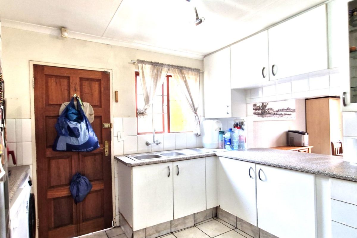 A functional kitchen featuring white cabinetry, laminate countertops, a double basin sink, and tiled flooring, offering a practical layout with potential for modernization.