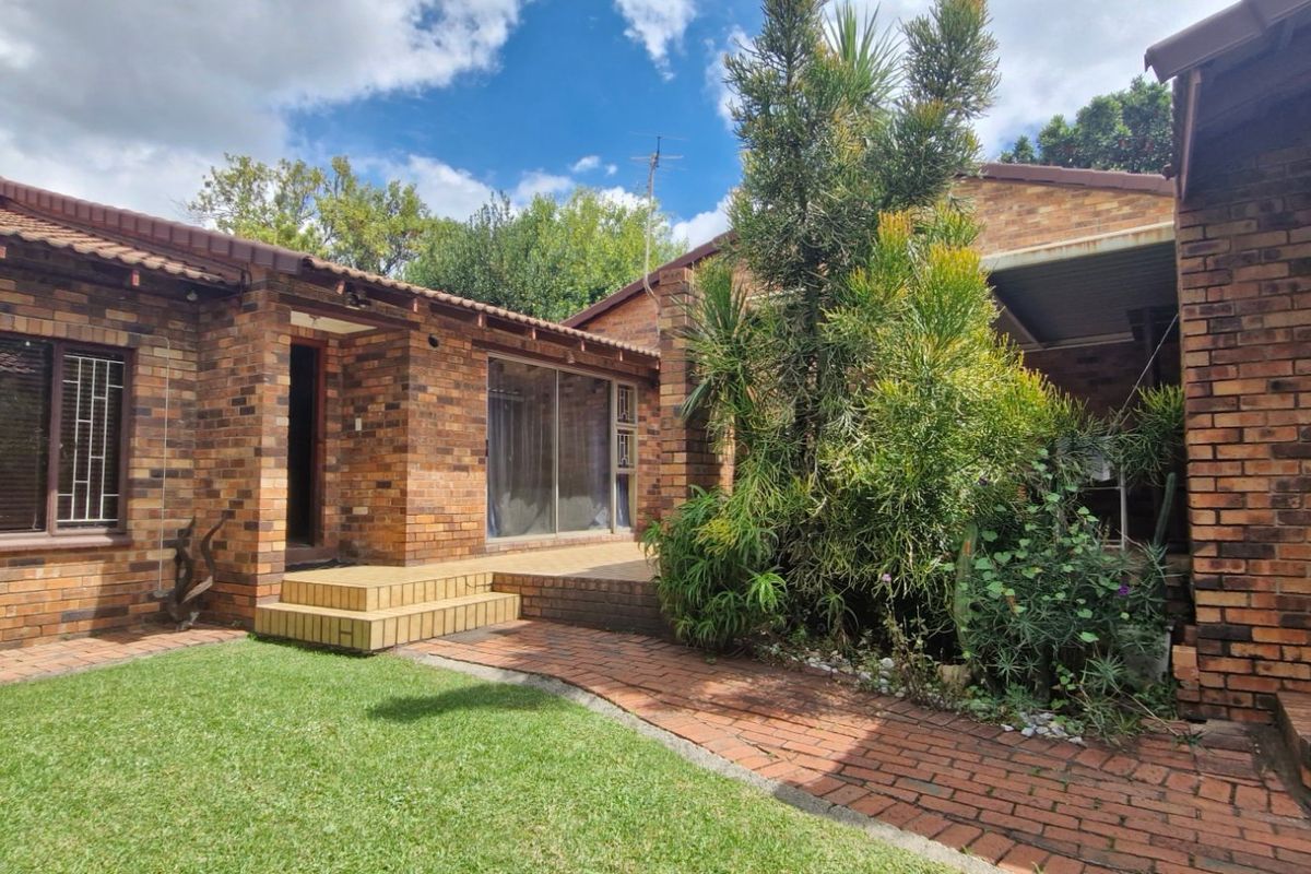 Rear view of a face brick townhouse featuring a paved walkway, tiled patio area, and sliding glass doors leading into the home.