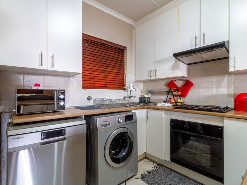 Compact kitchen featuring white cabinetry, laminate countertops, tiled backsplash, and integrated appliances including an oven, hob, and extractor fan.