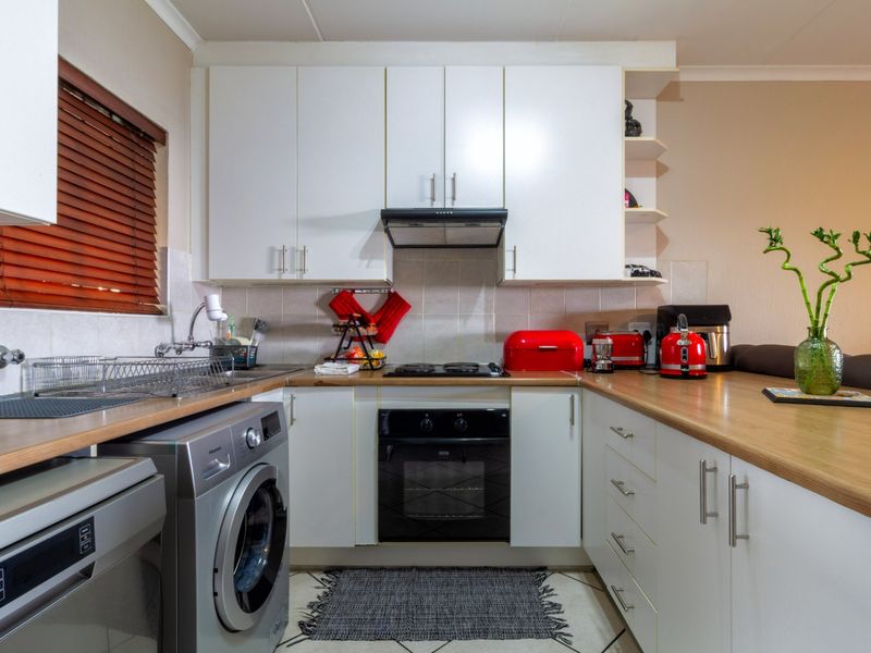Compact kitchen featuring white cabinetry, wood-look laminate countertops, built-in oven, electric hob, extractor fan, and tiled backsplash with integrated laundry plumbing.
