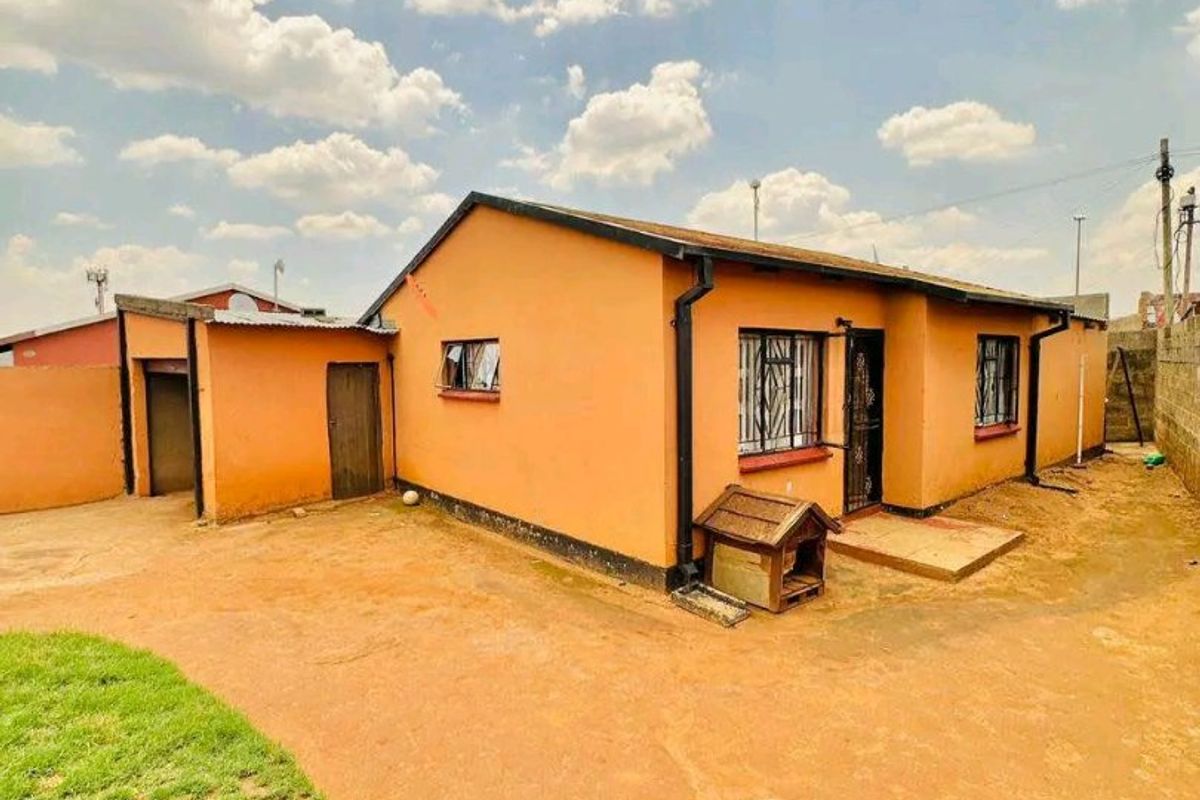 Rear view of a detached house featuring a simple exterior, security bars on windows, and a large open yard area.