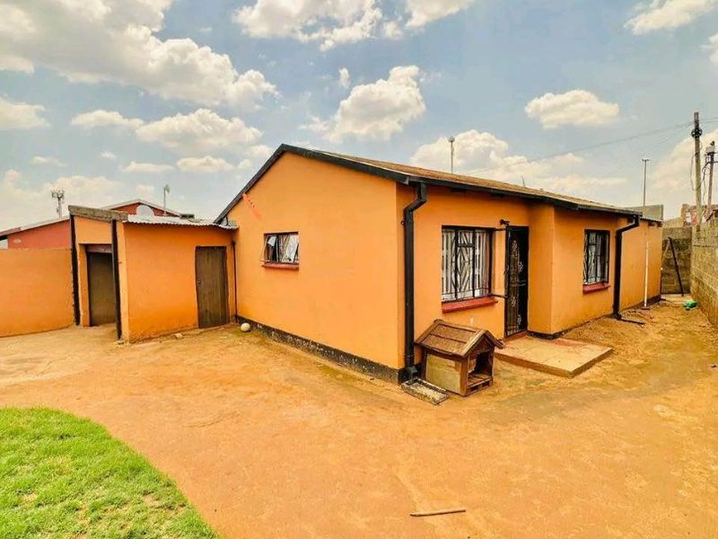 Rear view of a detached house featuring a simple exterior, security bars on windows, and a large open yard area.