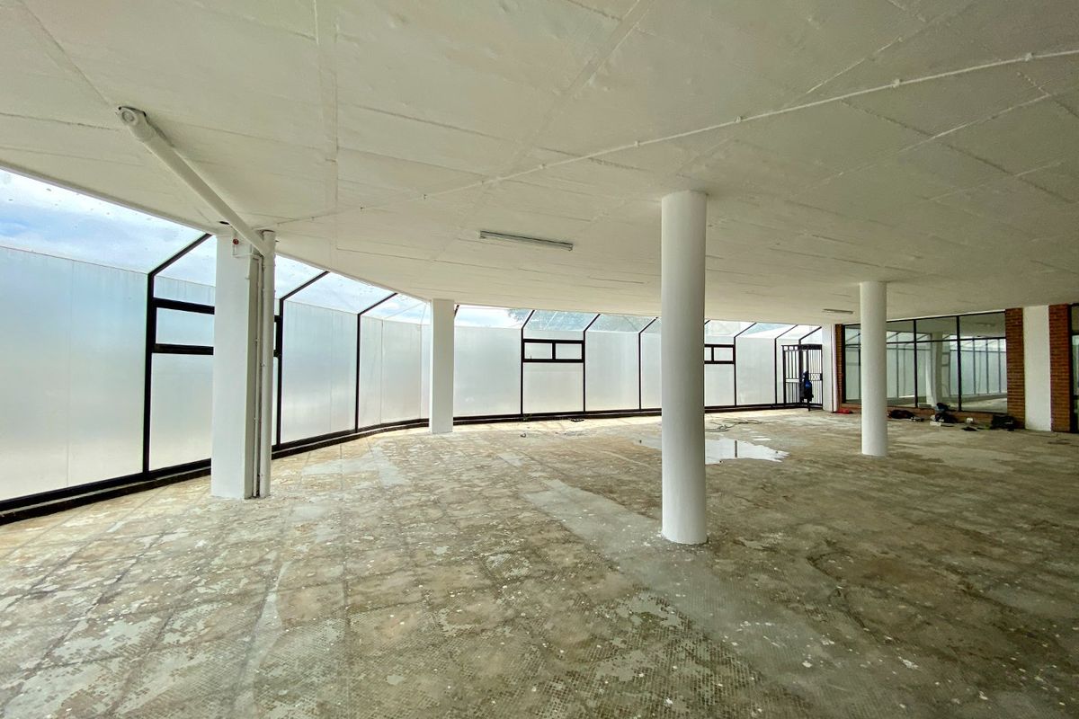 A large, vacant open-plan commercial space featuring structural columns, extensive glass paneling, and worn flooring, offering a blank canvas for renovation.