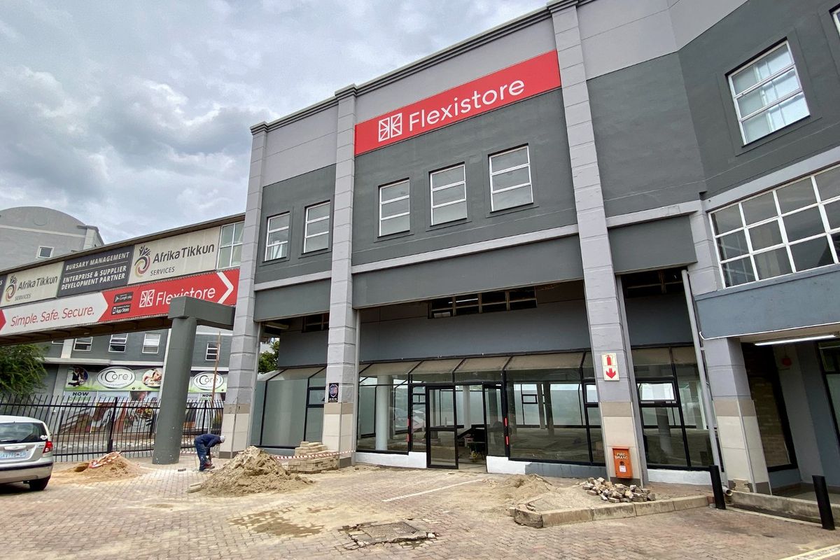 Front exterior view of a commercial building featuring glass storefront windows, prominent signage, and ongoing paving work in the driveway area.