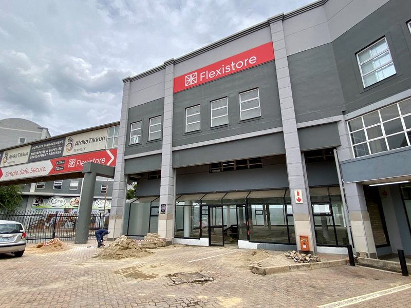 Front exterior view of a commercial building featuring glass storefront windows, prominent signage, and ongoing paving work in the driveway area.
