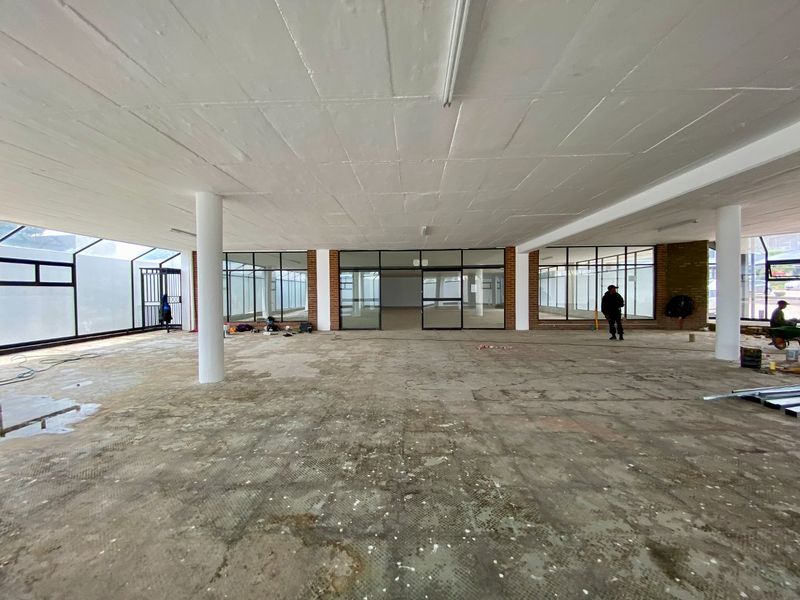 A large, open-plan commercial space featuring exposed concrete flooring, structural columns, and extensive aluminium-framed glass partitioning, currently in a shell condition.