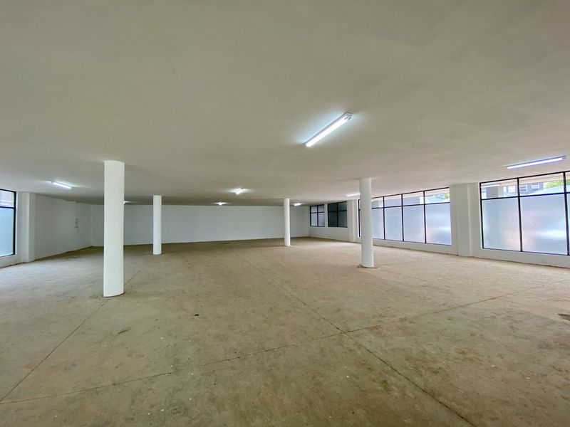 Spacious open-plan commercial area featuring structural columns, large windows providing natural light, and durable concrete flooring, suitable for various business configurations.