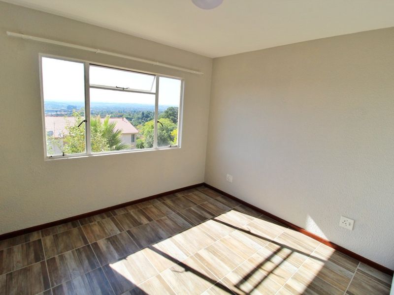 A bright, empty bedroom featuring tiled flooring, neutral walls, and a large window offering scenic views.