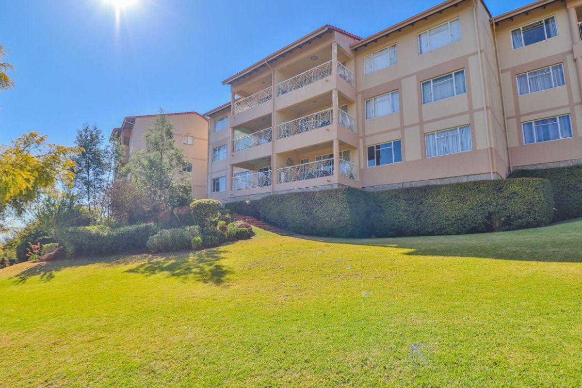 A view of the apartment building exterior featuring multiple levels of balconies with decorative railings, set against a well-maintained lawn and garden area.