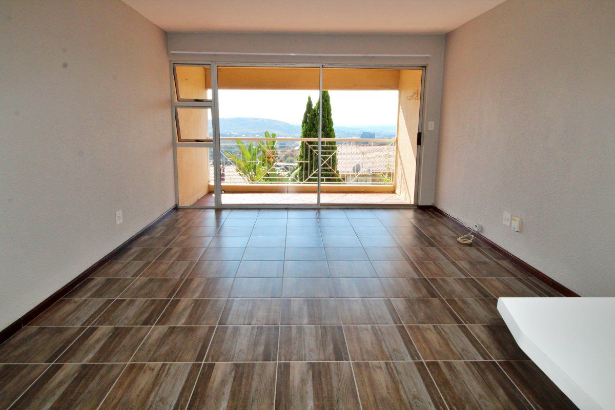 An empty living room featuring wood-look tiled flooring and a large sliding glass door that opens onto a balcony with scenic views.