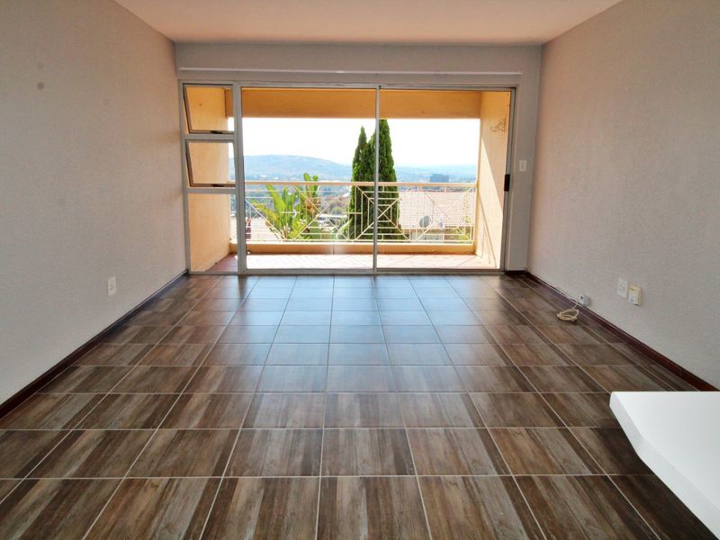 An empty living room featuring wood-look tiled flooring and a large sliding glass door that opens onto a balcony with scenic views.