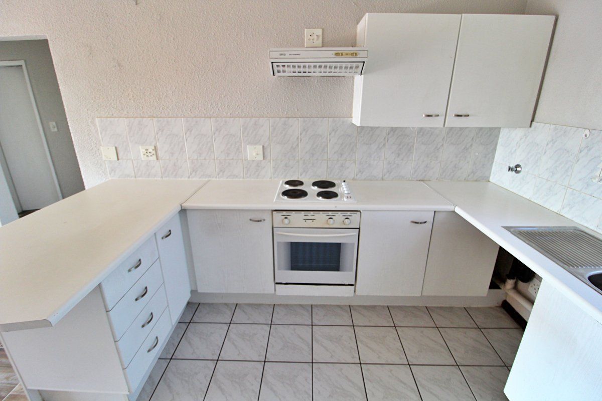 A functional kitchen featuring white built-in cabinetry, an electric stove with oven, extractor fan, tiled backsplash, and tiled flooring.