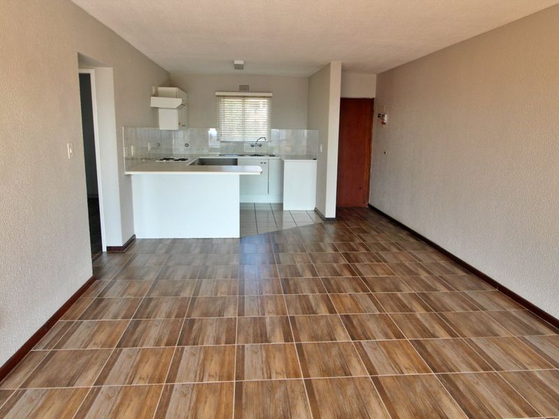 An open-plan living and kitchen area featuring wood-look tiled flooring, neutral walls, and a functional kitchen layout with built-in cabinetry and appliances.