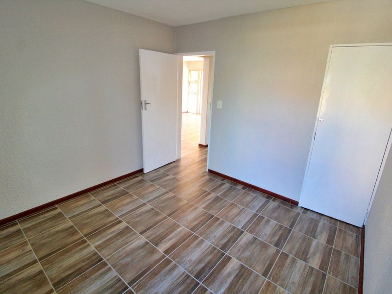 An empty bedroom featuring modern wood-look tiled flooring, a built-in cupboard, and neutral wall finishes.