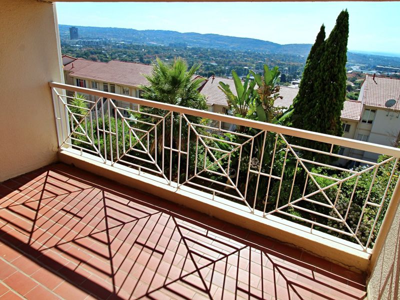 A covered balcony featuring a decorative metal balustrade and tiled flooring, offering elevated views of the surrounding neighborhood and landscape.