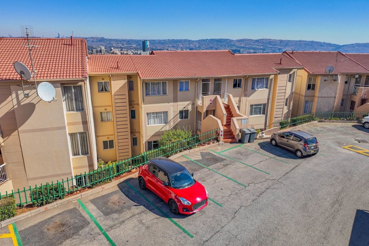 Aerial view of an apartment complex featuring terracotta tiled roofs, exterior staircases, and an asphalt parking area with marked bays.