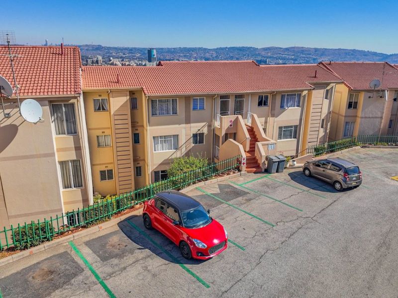Aerial view of an apartment complex featuring terracotta tiled roofs, exterior staircases, and an asphalt parking area with marked bays.
