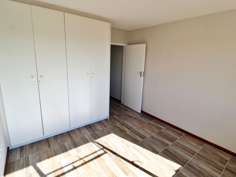 A bright, empty bedroom featuring modern wood-look tiled flooring and ample built-in cupboard storage space.